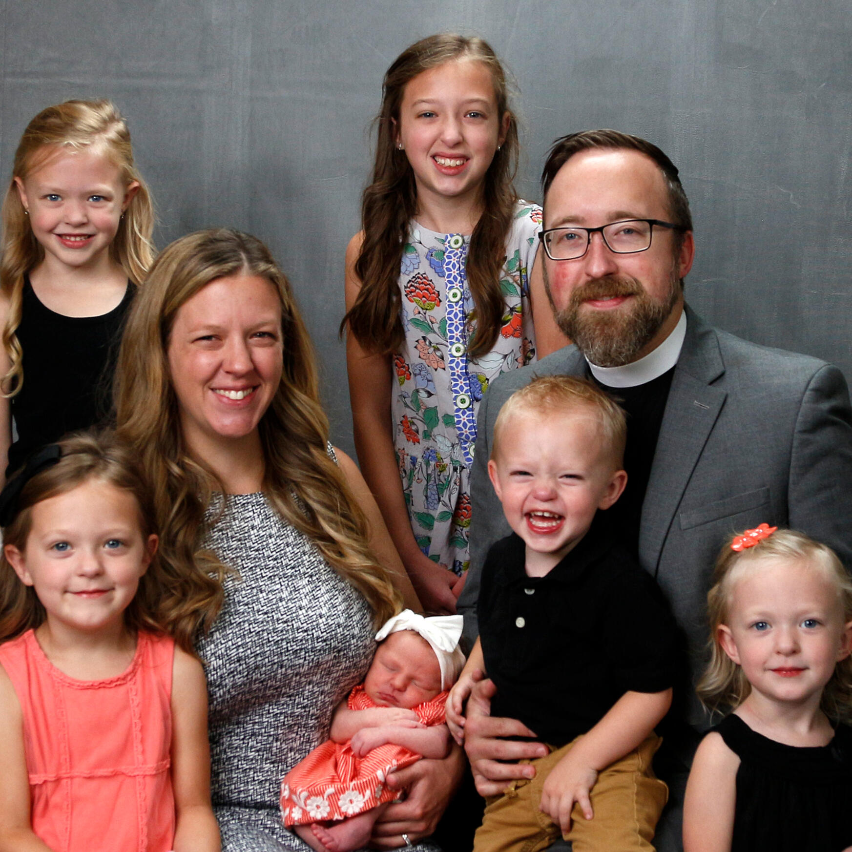 Family portrait of Pastor David Clark of Trinity Lutheran Church in Odebolt, Iowa, wearing a clerical collar, pictured with his wife and their six children of various ages, including a newborn baby.