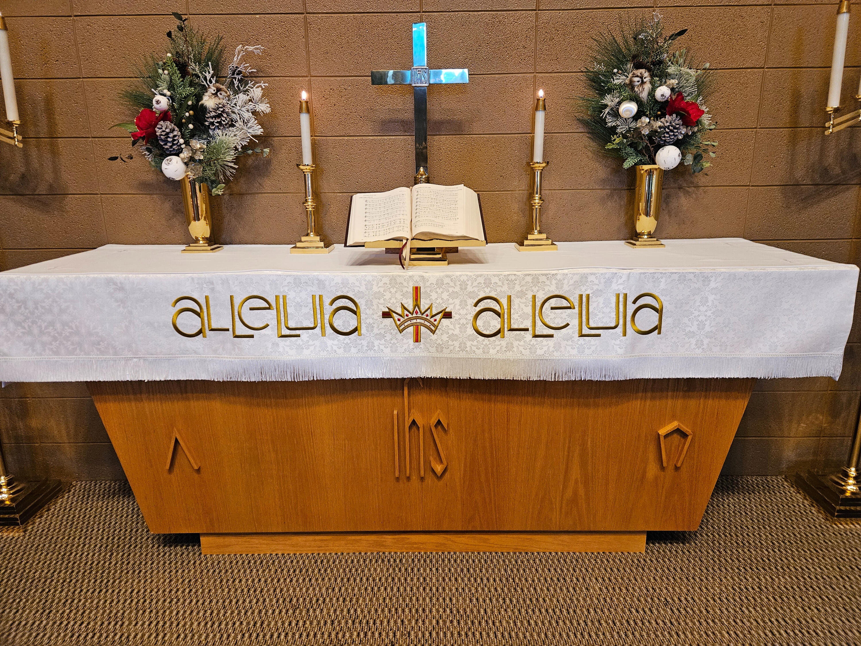The altar at Trinity Lutheran Church in Odebolt, Iowa, with winter greenery, candles, a cross, an open hymnal, and white paraments.